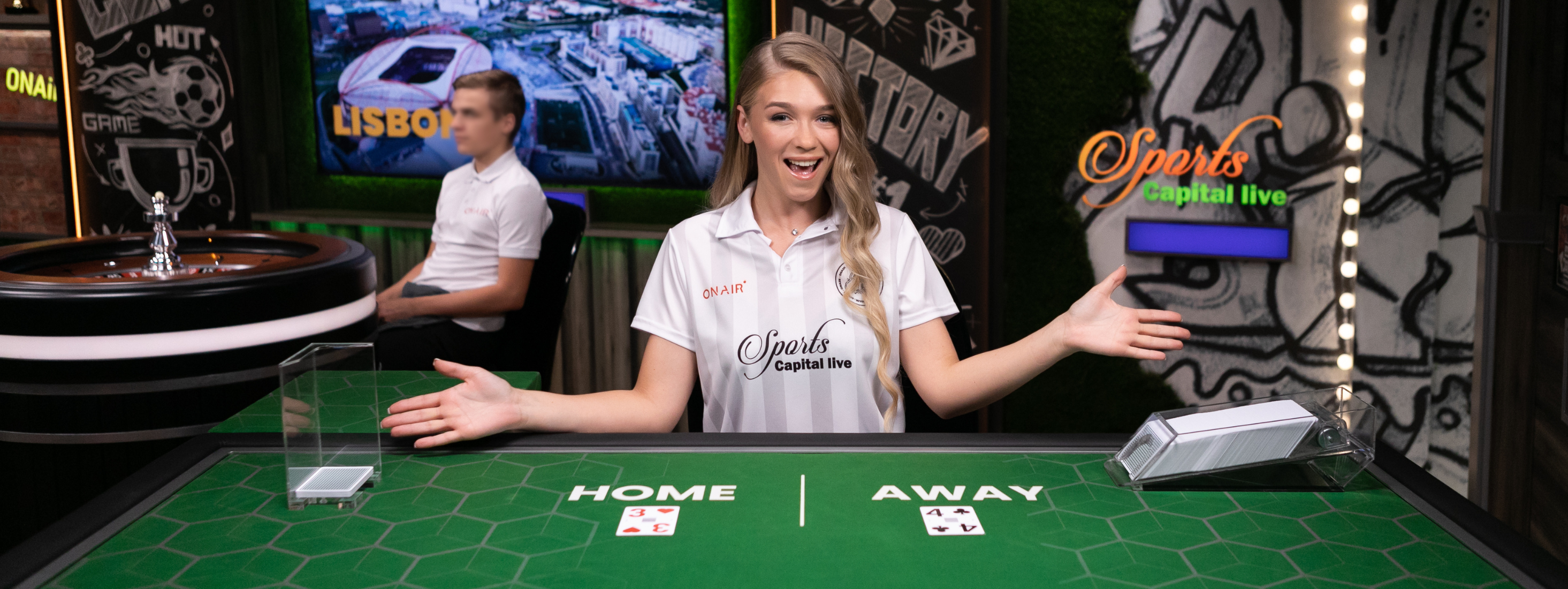 Female game presenter behind a table in Card Matchup, with 'Home' and 'Away' cards set out on the green felt table.