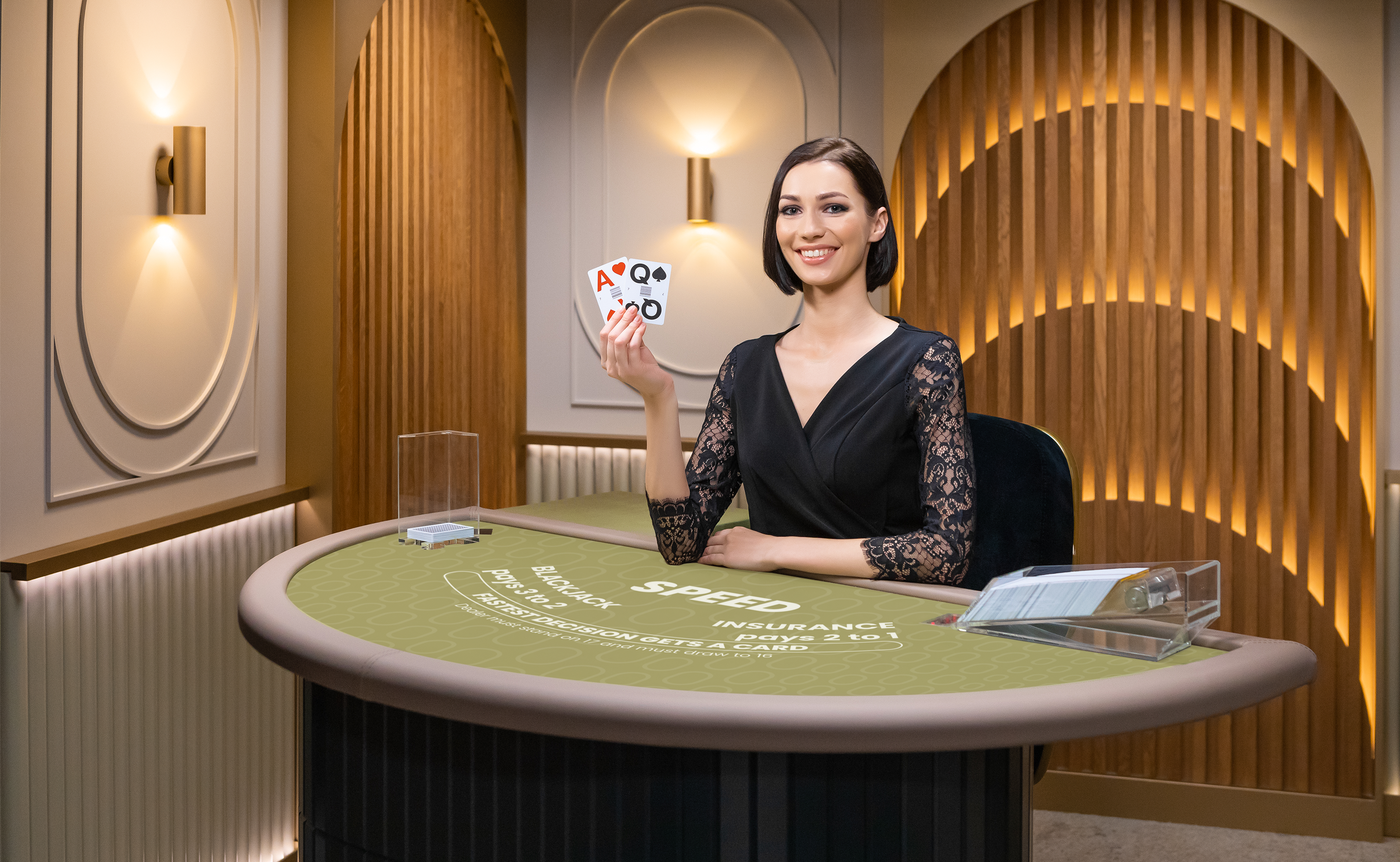Female game presenter behind a Blackjack table holding up 2 cards in a game of Speed Blackjack.