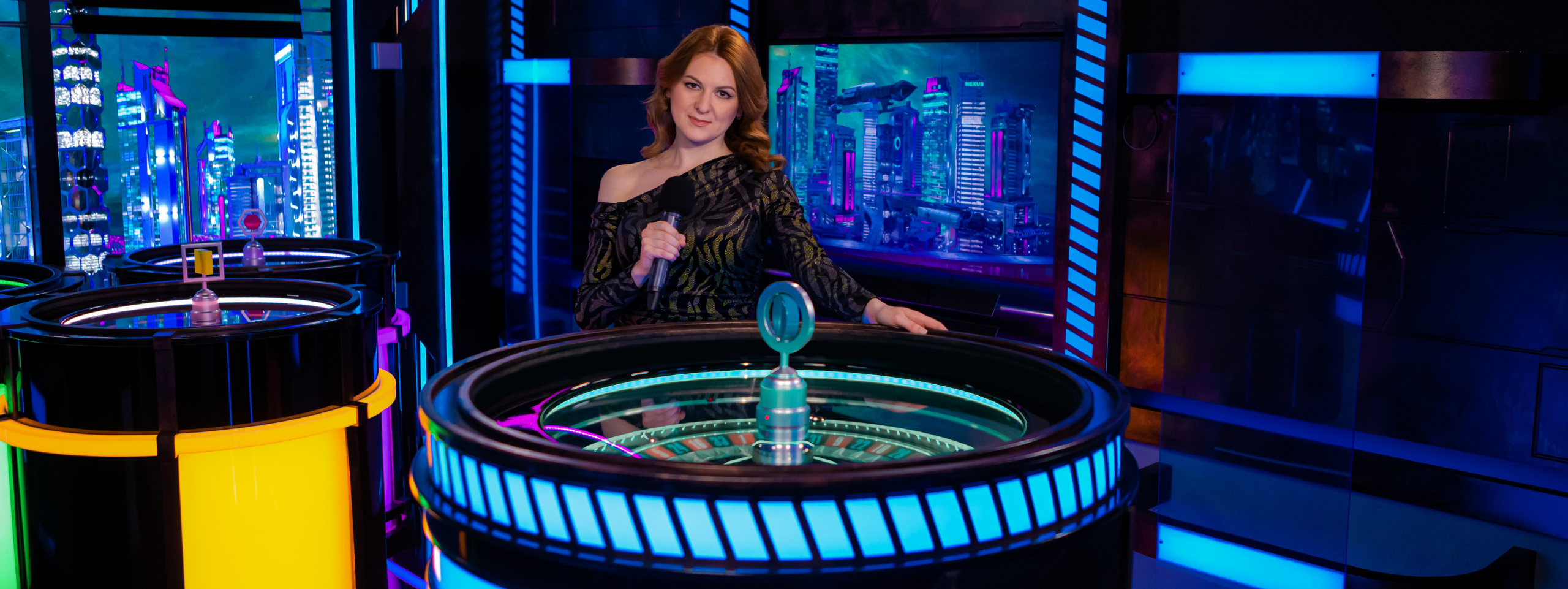 Female game presenter in front of roulette wheel in Nexus Roulette.